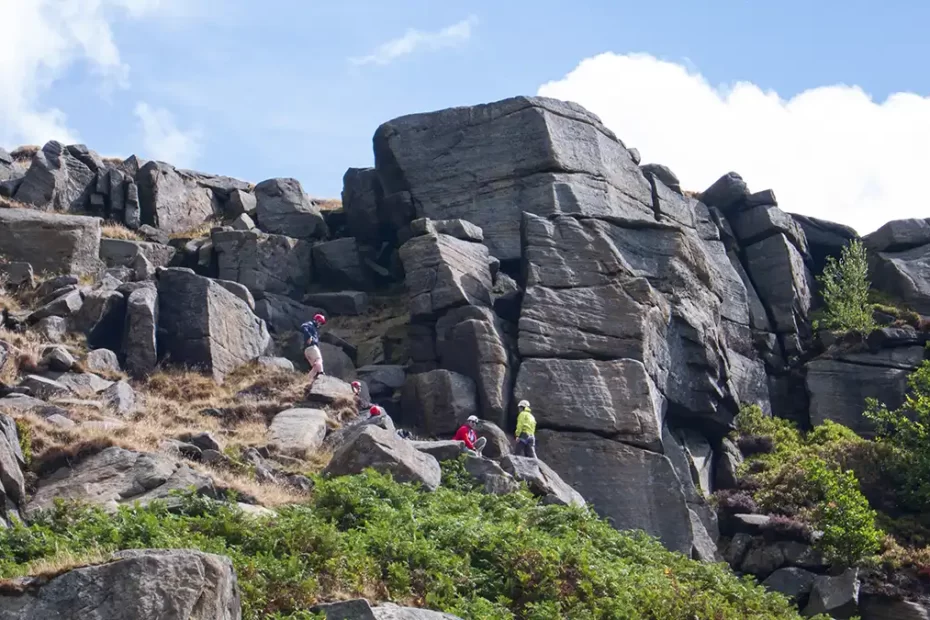 A group of climbers tackle a route up the gritstone face of Stanage viewed from below