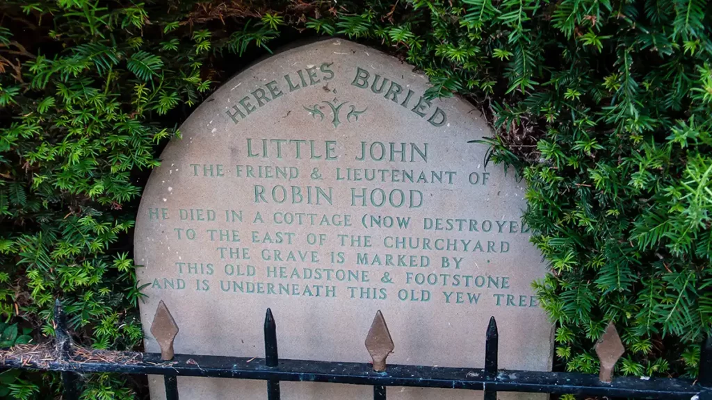 A headstone beside a tree proclaims "Here lies buried Little John, the friend and lieutenant of Robin Hood. He died in a cottage (now destroyed) to the east of the churchyard. The grave is marked by this old headstone and footstone and is underneath this old yew tree"