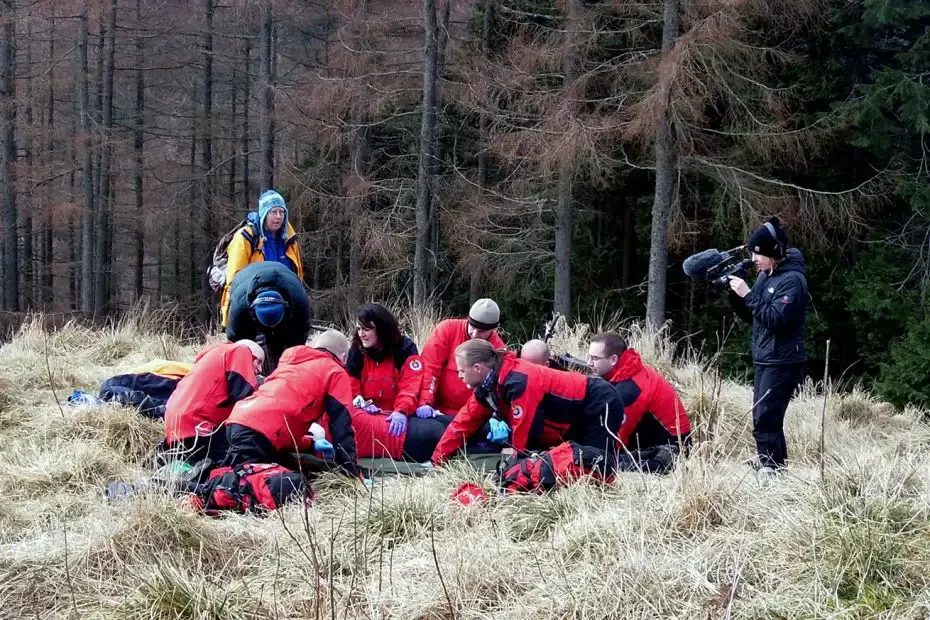 A mountain rescue team in operation. Two Land Rover Defender vehicles and a Transit van with a large radio mast park beside a lane in the mountain
