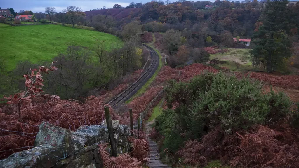 A footpath heads down steps at Mill Scar. A railway line runs below to the left.